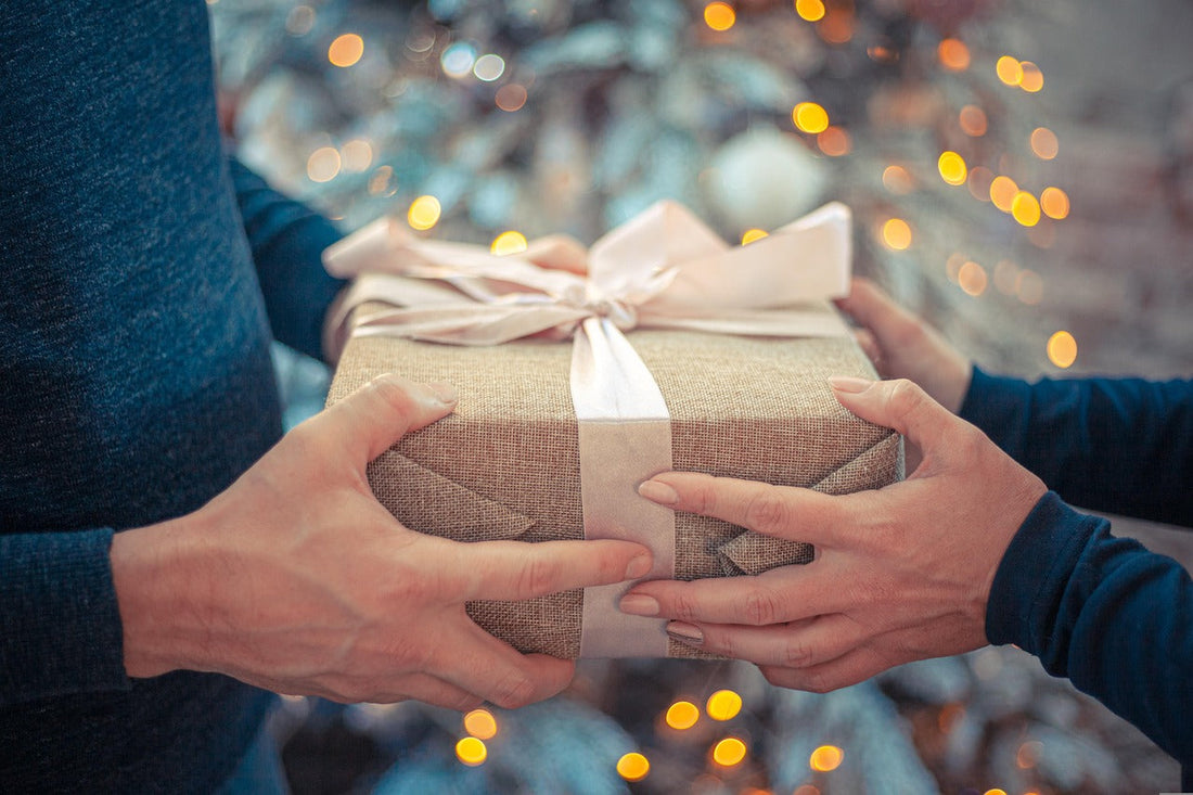 Zwei Menschen überreichen sich ein Geschenk vor Lichtern – symbolisch für persönliche und bedeutungsvolle Geschenke
