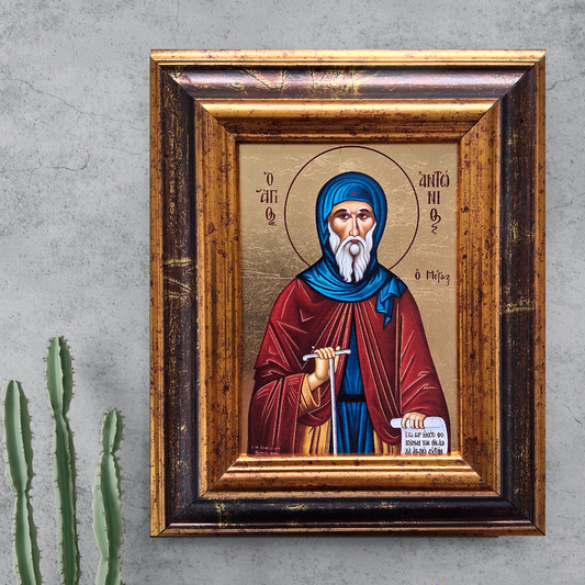 Ikone des Heiligen Antonius im verzierten Holzrahmen vor grauer Wand mit Kaktuspflanze.